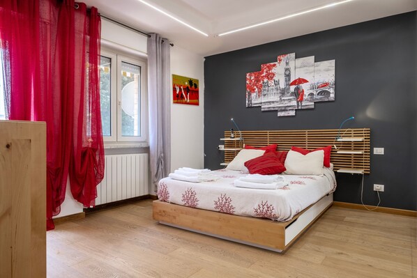 A bedroom with a bed, a window with curtains, a radiator, and artwork on the wall.