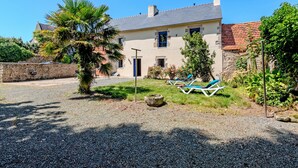 Una casa con un muro de piedra, una palmera y dos sillones azules en el patio.