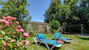 Dos sillones de descanso con toallas, un muro de piedra y rosas rosadas en flor en un jardín.