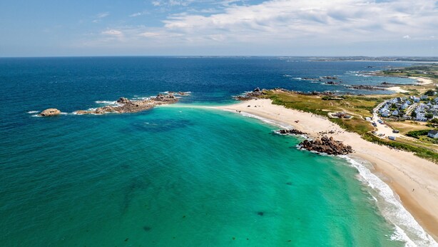 Vista aérea de una zona costera con playa, afloramientos rocosos y un pequeño poblado con casas.