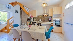 Una cocina moderna con armarios de madera, un comedor con una mesa preparada para cuatro comensales y una escalera que sube a un nivel superior.