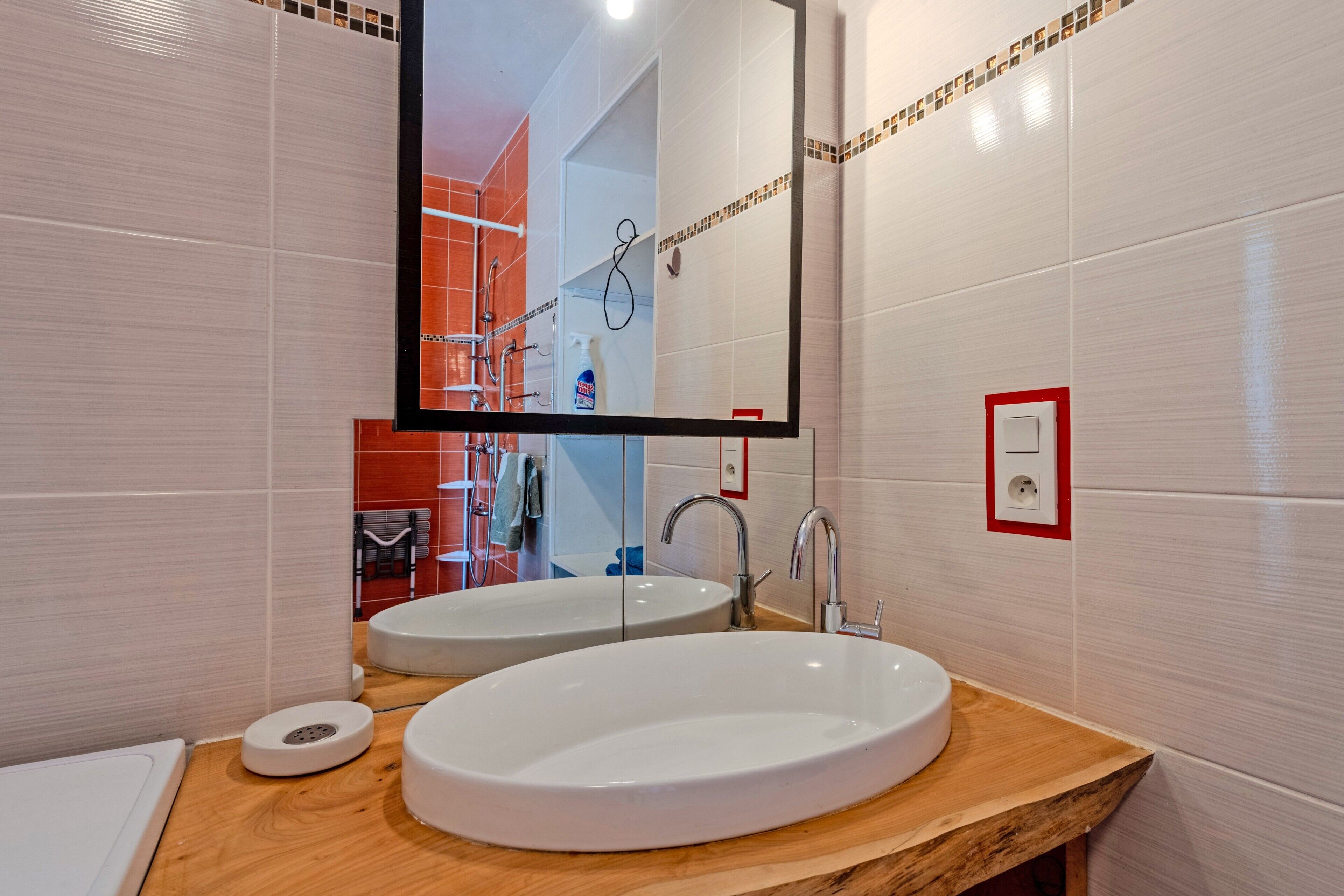 A bathroom with two sinks, a mirror, and a red-framed electrical outlet.