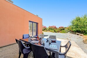 Un área de comedor al aire libre con mesa y sillas, una ventana y vista a un jardín.