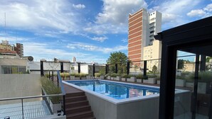 Un área de piscina en la azotea con vistas despejadas al horizonte de la ciudad, incluyendo un edificio alto y una estructura más pequeña.
