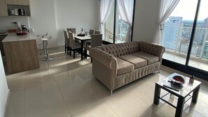 Una sala moderna con un sofá seccional beige, una mesa de comedor con sillas y una zona de cocina con armarios y encimera.