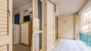Una puerta corredera abierta que da a un balcón con piso de baldosas y vista a un edificio.