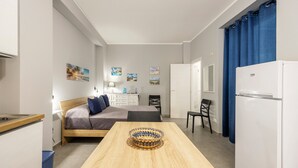 Una habitación pequeña con cama, mesa de comedor, kitchenette y refrigerador.