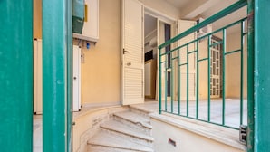 Una escalera conduce a un cuarto con barandilla verde, una puerta y un equipo de aire acondicionado de pared.