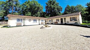 Un bâtiment à deux étages avec une cour en gravier, une fontaine et un banc.