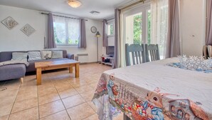 Un salon avec un canapé, une table en bois, un lit recouvert d’une couverture colorée, une lampe et une fenêtre avec des rideaux.