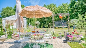 Un jardín con una mesa y sillas, un paraguas de paja y un pabellón.