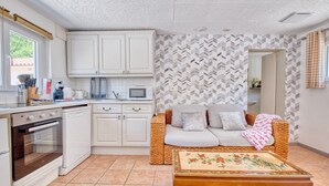 Una cocina compacta con armarios blancos, un microondas y una mesa de comedor con mantel floral.