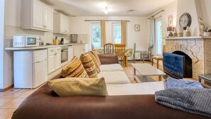 A living room with a sofa, TV, fireplace, kitchen area, and dining table. - Apartment 'Stag' with Shared Pool, Wi-Fi and Air Conditioning (Bergerac)