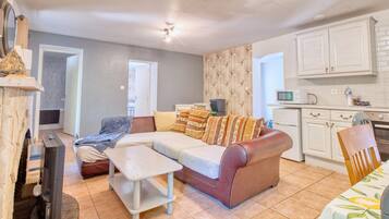 Una sala de estar con sofá, televisión, chimenea y una zona de cocina con armarios y microondas.
