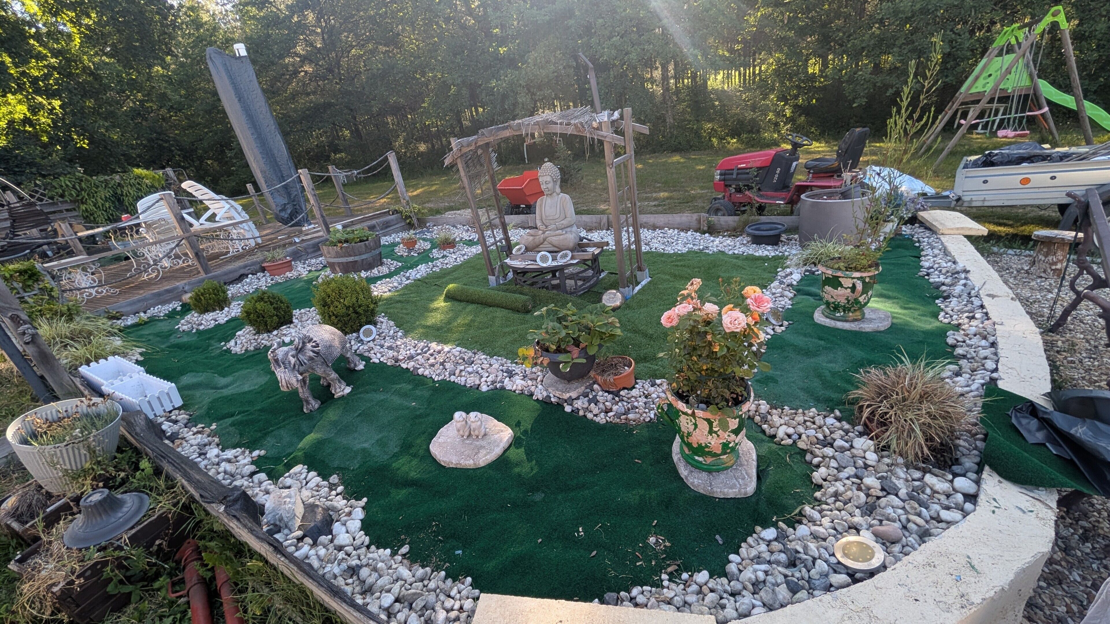 Een tuin met een Boeddhabeeld, een schommel en een grasmaaier.