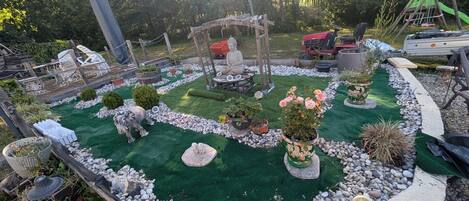 A garden with a Buddha statue, a swing set, and a lawnmower.