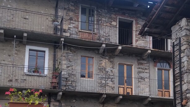 A stone building with multiple balconies, wooden doors, and potted plants. - The House in the Green (Lortallo)