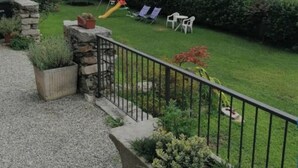 A courtyard with a grassy lawn, a children's play area, and a stone wall. - The House in the Green (Lortallo)