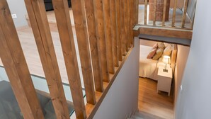 Una scala moderna con ringhiere in legno, pavimento in vetro e una camera da letto con un letto, comodino e lampada.