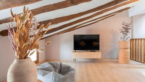 Una stanza con soffitto in legno, una televisione su un mobile di legno, un cesto di vimini e una pianta.