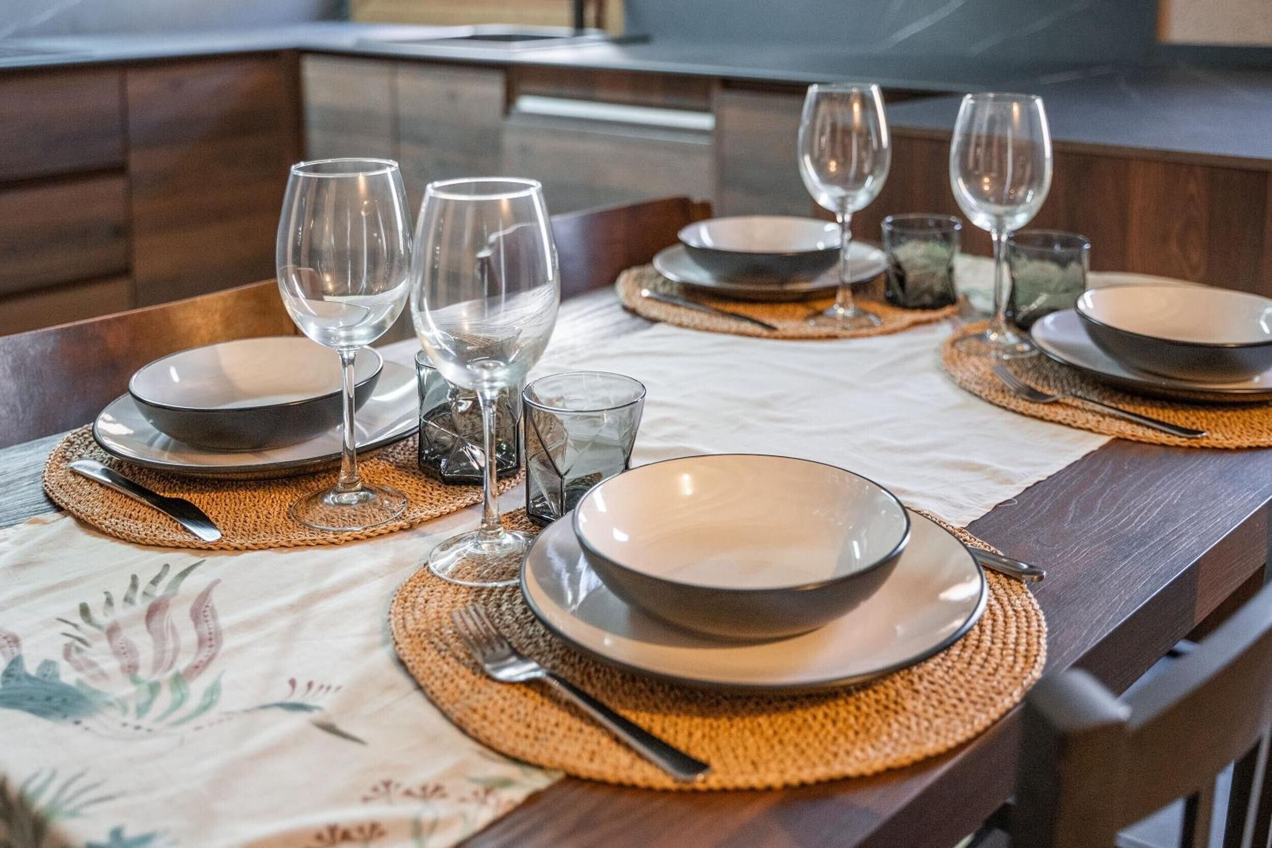 Una mesa de comedor dispuesta con platos, vasos y cubiertos, con un mantel individual debajo de cada juego.