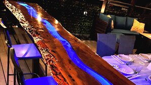 Eine Bar mit einer langen Holztresen, blauen Barhocker und einer blau beleuchteten Wand.