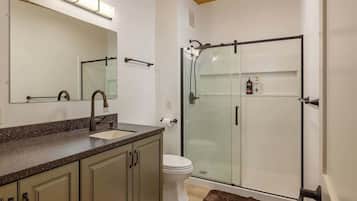 Een badkamer met een douchecabine van glas, een wastafel met een moderne kraan en een toilet.