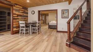 A modern interior with a wooden ceiling, a dining area with a table and chairs, a staircase, and a bed in the background. - Residential Area Ski Chalet by Creek - Sleeps 6 (Girdwood)