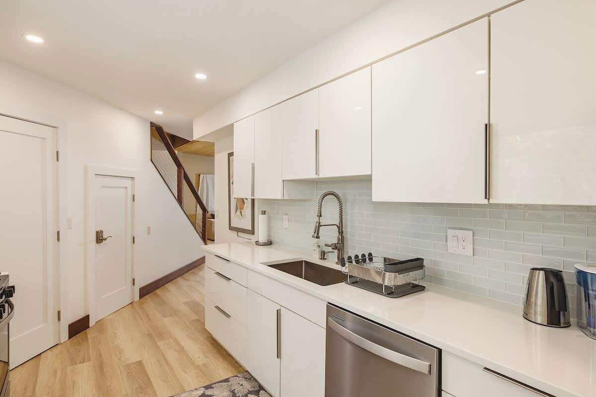 A modern kitchen with white cabinets, a stainless steel dishwasher, and a tiled backsplash.