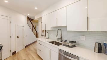 A modern kitchen with white cabinets, a stainless steel dishwasher, and a tiled backsplash.