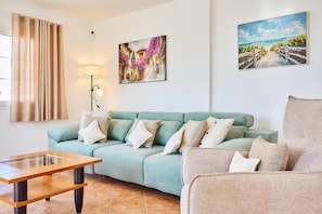 Uma sala de estar com um sofá verde-água, uma mesa de centro de madeira, um abajur e duas pinturas na parede.