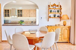 A dining area with a round table, six chairs, a bowl, a wooden cabinet, and a shelf with decorative items.