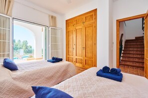 A hotel room with two beds, a wooden wardrobe, and a view of the outside.