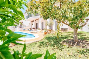 Uma área de piscina com espreguiçadeiras, uma árvore e um edifício com varandas.