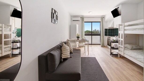 Una habitación moderna con sofá, literas, mesa de comedor y vistas al exterior.