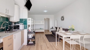 Una cocina moderna con microondas, pileta y alacenas, un comedor con mesa y sillas, y una cama litera al fondo.