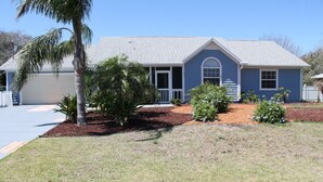 A single-story house with a blue exterior, a covered porch, and a small front yard with landscaping.