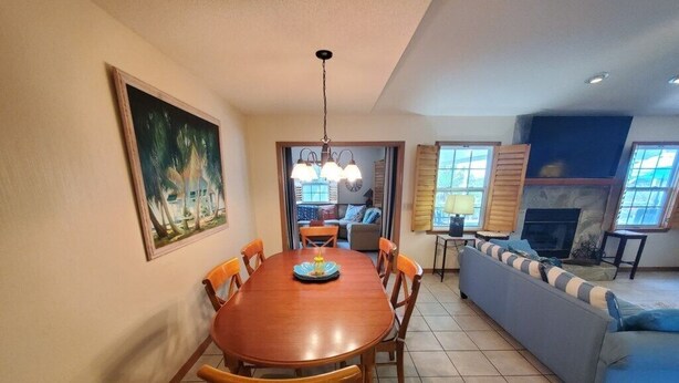 A dining area with a wooden table and chairs, a painting on the wall, and a sofa in the background.