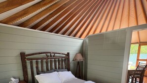 A wooden bed with a headboard, a bedside table, and a lamp. - Shoreline Yurt @ Daggett Lake (Warrensburg)