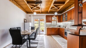 A modern kitchen with wooden cabinets, a dining area with a table and chairs, and a view of the outdoors through a glass door. - Hillside Apartment Gjirokaster by PikHost (Gjirokastër)
