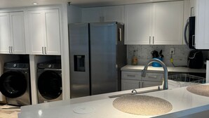 A modern kitchen with white cabinets, stainless steel appliances, and a central island with a sink. - Beachfront 2BR/2BA Condo on Hutchinson Island w/ Private Garage (Fort Pierce)