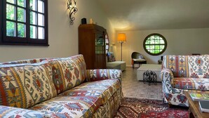 A cozy living room with patterned sofas, a wooden cabinet, a round window, and a floor lamp. - Villa Gioia on the Euganean Hills (Torreglia)