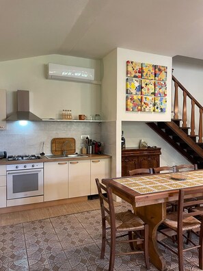 Une cuisine équipée d’une cuisinière, d’un évier et de meubles de rangement en bois. On y trouve une table à manger avec des chaises, ainsi qu’un escalier menant à un autre niveau.