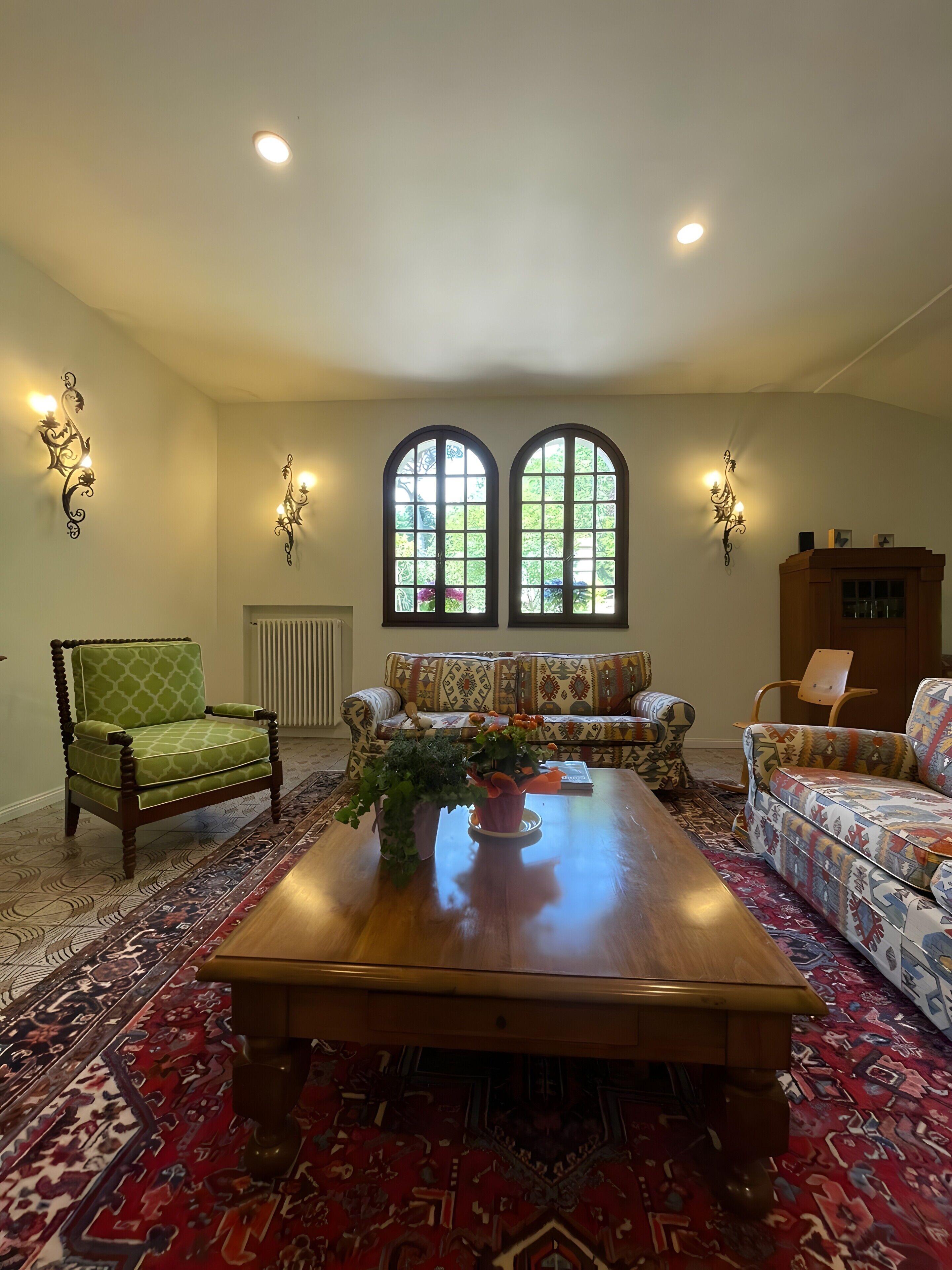 A living room with a large wooden coffee table, patterned sofas, a green armchair, and decorative wall sconces.