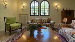 A living room with a large wooden coffee table, patterned sofas, a green armchair, and decorative wall sconces. - Villa Gioia on the Euganean Hills (Torreglia)