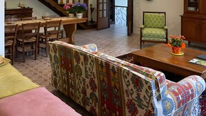 A spacious living area with a wooden staircase, a dining table, a sofa, and a green patterned armchair. - Villa Gioia on the Euganean Hills (Torreglia)