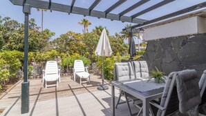 Un espacio al aire libre cubierto con una mesa, sillas, una pérgola y un muro de piedra.