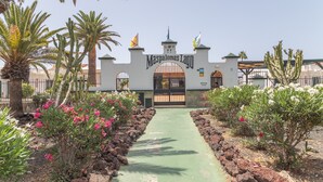 Una puerta con la inscripción 'Maspalomas Lago' en la parte superior, rodeada de cactus y plantas con flores.