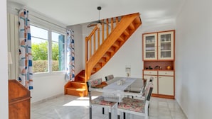 A dining area with a table, chairs, a staircase, and a cabinet. - Holiday Home 'Maison Ker Hélène' with Private Terrace, Wi-Fi and Air Conditioning (Guérande)