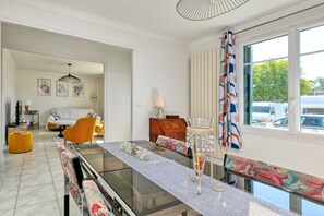 A modern living room with a glass-top dining table, a sofa, and a wooden cabinet. - Holiday Home 'Maison Ker Hélène' with Private Terrace, Wi-Fi and Air Conditioning (Guérande)